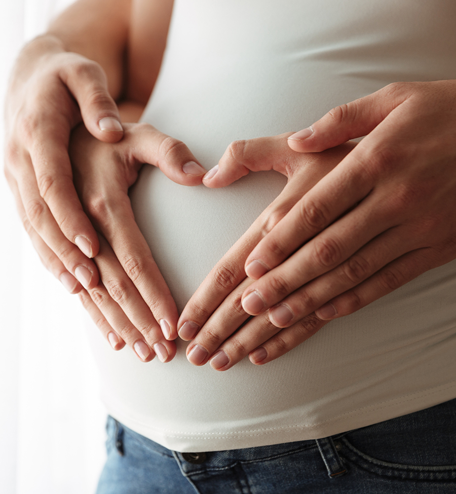 Close up portrait of man’s and woman’s hands Close up portrait of man's and woman's hands making heart gesture over pregnant belly indoors